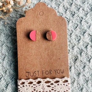 May include: A pair of wooden earrings with pink resin half circles. The earrings are displayed on a brown card with the text "Just for you" and a white lace trim.