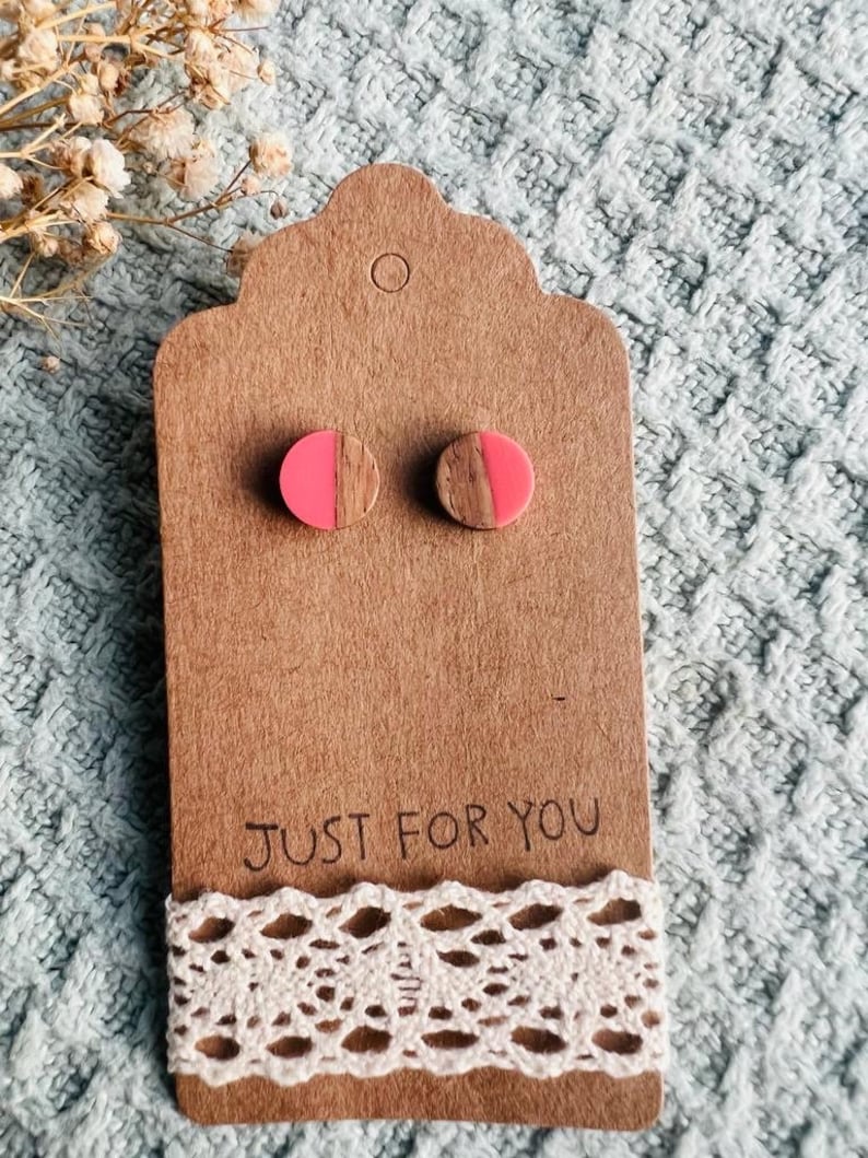 May include: A pair of wooden earrings with pink resin half circles. The earrings are displayed on a brown card with the text "Just for you" and a white lace trim.