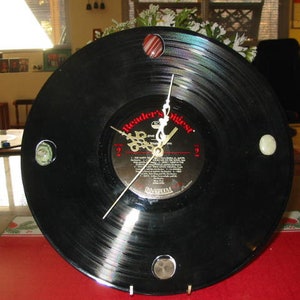 May include: A black vinyl record clock with a white clock face and gold hands. The clock face has the text "Reader's Digest" and "The Best of Country" printed on it. The clock is decorated with colorful stones around the edge.
