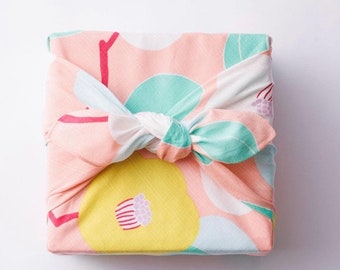 May include: A pink and white fabric gift wrap with a floral pattern. The fabric is tied with a white knot and has a yellow, green, and pink floral design.