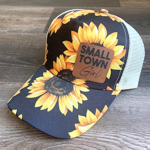 May include: Black trucker hat with a sunflower pattern and a brown leather patch that says "Small Town Girl".