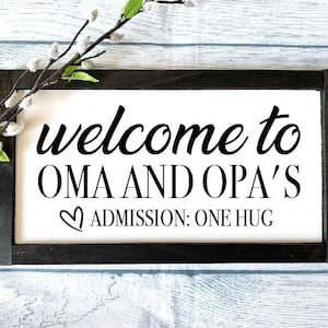May include: A black framed sign with white text that reads "welcome to Oma and Opa's" with a heart symbol and the text "Admission: One Hug".