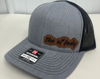 Peut inclure: Un chapeau de camionneur gris et noir avec un patch en cuir marron qui dit "the ol' lady". Le chapeau est fabriqué par Richardson 112 et est réglable.
