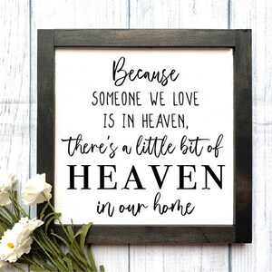 May include: Black framed sign with white background and black text that reads "Because someone we love is in heaven, there's a little bit of heaven in our home".