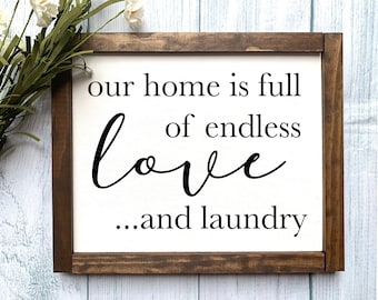 May include: A framed sign with a white background and black text that reads "our home is full of endless love...and laundry". The frame is brown wood.