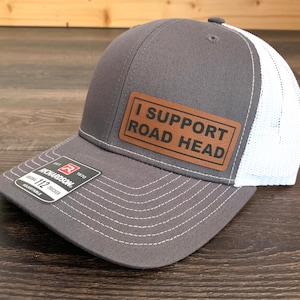 May include: A gray and white trucker hat with a brown leather patch that says "I Support Road Head".