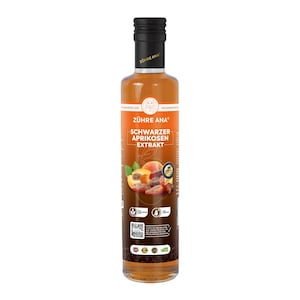 Op de afbeelding: Een heldere glazen fles met een zwarte dop, gevuld met een licht amberkleurige vloeistof. Het etiket toont de tekst "ZÜHRE ANA" en "SCHWARZER APRIKOSEN EXTRAKT" met afbeeldingen van abrikozen. Waarschijnlijk een voedingsproduct.