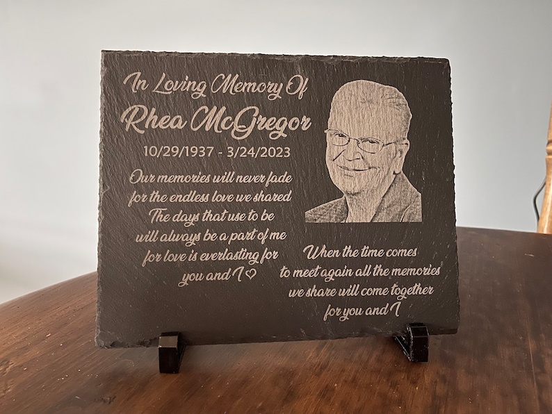K&ouml;nnte beinhalten: Eine schwarze Schiefertafel mit einem Foto einer Person und einer eingravierten Botschaft. Die Botschaft lautet "In liebevoller Erinnerung an Rhea McGregor 10/29/1937 - 3/24/2023 Unsere Erinnerungen werden nie verblassen f&uuml;r die unendliche Liebe, die wir teilten Die Tage, die fr&uuml;her waren, werden immer ein Teil von mir sein, denn Liebe ist ewig f&uuml;r dich und mich Wenn die Zeit kommt, uns wieder zu treffen, werden all die Erinnerungen, die wir teilen, f&uuml;r dich und mich zusammenkommen".