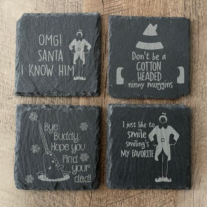 May include: Four black slate coasters with white engraved text and images. The coasters feature quotes from the movie Elf, including "OMG! Santa I know him", "Don't be a cotton headed ninny muggins", "Bye Buddy, hope you find your dad!" and "I just like to smile, smiling's my favorite".