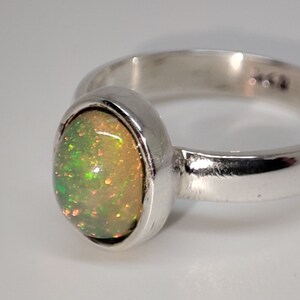 May include: A silver ring with an oval-shaped opal gemstone. The opal is a light green color with a hint of orange.