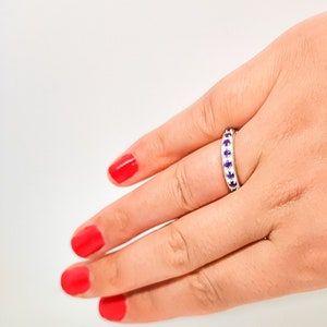 Peut inclure: Une bague en argent avec une rangée de petites pierres précieuses violettes.
