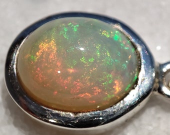 May include: A silver pendant with a round opal gemstone. The opal has a white base with flashes of green, red, and orange.