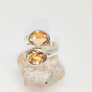 Könnte beinhalten: Ein silberner Ring mit zwei ovalen Topas-Edelsteinen. Der Ring liegt auf einem weißen Hintergrund.