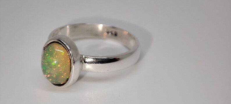 May include: A silver ring with an oval-shaped opal gemstone. The opal is a light green color with a hint of orange.