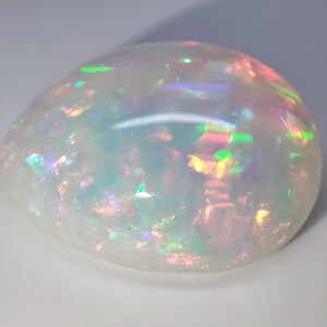 May include: A white opal gemstone with iridescent flashes of green, blue, and pink.