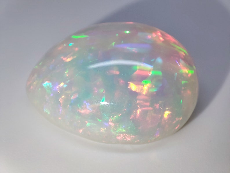 May include: A white opal gemstone with iridescent flashes of green, blue, and pink.