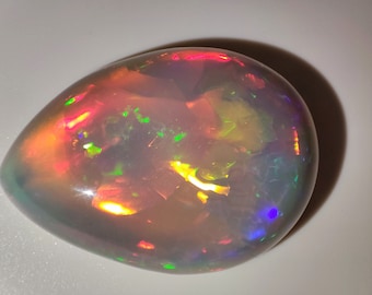 May include: A teardrop-shaped opal gemstone with a white base and iridescent flashes of green, red, orange, and blue.