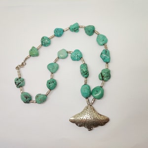 Peut inclure: Un collier de pierres turquoise avec un pendentif en argent en forme d'éventail. Le collier est composé de pierres turquoise de forme irrégulière et de perles d'argent.