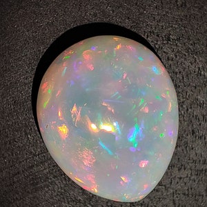 May include: A white opal gemstone with iridescent flashes of color, including green, blue, and pink.