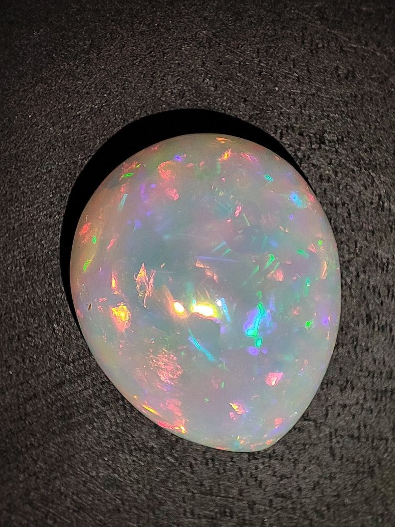 May include: A white opal gemstone with iridescent flashes of color, including green, blue, and pink.