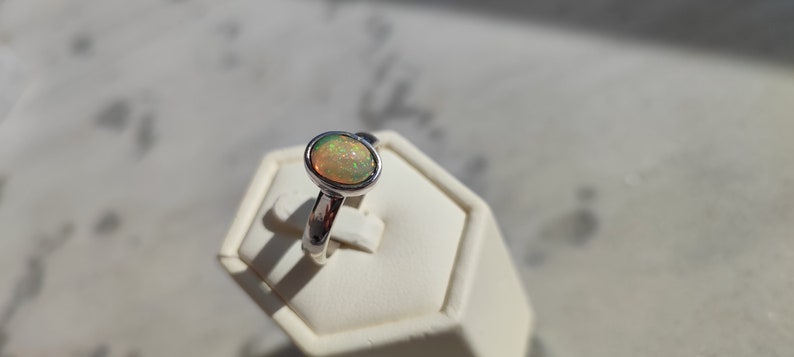 May include: A silver ring with a light green opal gemstone. The ring is on a white display stand.