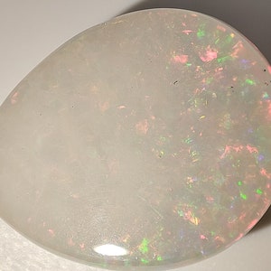 May include: A white opal gemstone with a teardrop shape and iridescent flashes of pink, green, and blue.