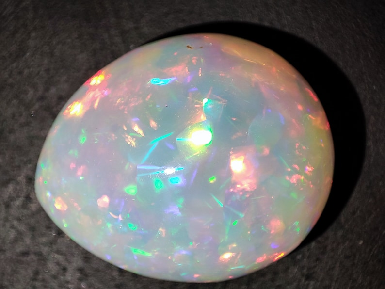 May include: A white opal gemstone with iridescent flashes of green, blue, pink, and orange.