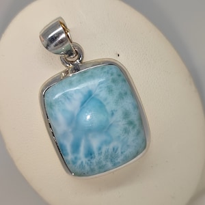May include: A silver pendant with a light blue, rectangular, cabochon gemstone. The gemstone has a unique, swirling pattern.