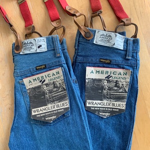 May include: Two pairs of blue denim jeans with red braces. Both pairs have a Wrangler American Legend label and a Wrangler Blues label that says "The new wave is old wave".