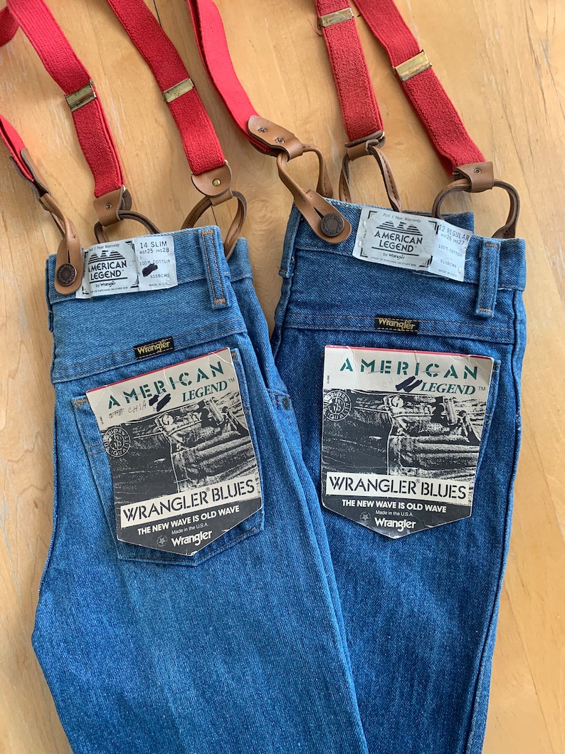 May include: Two pairs of blue denim jeans with red braces. Both pairs have a Wrangler American Legend label and a Wrangler Blues label that says "The new wave is old wave".