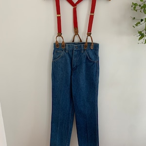 May include: Red braces with brown leather accents and a pair of blue denim jeans.