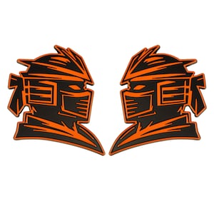 May include: Two black and orange stylized helmet-shaped designs. Each design features a detailed outline of a helmet with angular features and a face mask. The helmets are symmetrical and appear to be made of a rubbery material.
