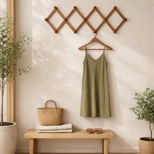 K&ouml;nnte beinhalten: Minimalistische Inneneinrichtung mit einer Holzbank, einer geflochtenen Tragetasche und einem gr&uuml;nen Kleid an einem Holzkleiderb&uuml;gel. Ein erweiterbarer Kleiderhaken aus Holz ist an der Wand befestigt. Zwei kleine Topfpflanzen und ein Teppich.
