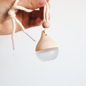 May include: A wooden and glass diffuser with a white string hanging from it. The diffuser is shaped like a teardrop and has a wooden top.