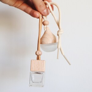 May include: A wooden car air freshener with a clear glass bottle and a wooden top. The air freshener is hanging from a beige and brown string.