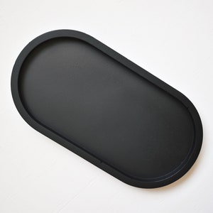 May include: A black oval-shaped tray with a smooth, matte finish. The tray is perfect for holding small items like jewelry, keys, or coins.