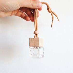 May include: A small, clear glass bottle with a wooden lid and a brown string attached. The bottle is hanging from the string.