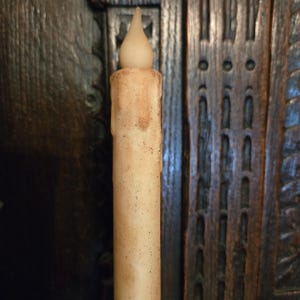 May include: A battery-operated, cream-colored candle with a realistic flame-shaped tip. The candle has a textured, aged appearance with brown spots and drips, suggesting a vintage aesthetic. The candle is designed to mimic the look of a traditional wax candle.