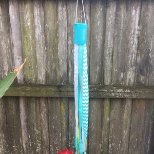 May include: A teal blue tin can with a string attached to it. The string has multiple ribbons attached to it, including white, yellow, and teal blue with a white chevron pattern.