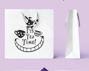 Può includere: Una borsa regalo bianca con manici neri e un design con un sorriso del Gatto del Cheshire, tazze da tè e il testo "It's Tea Time!"