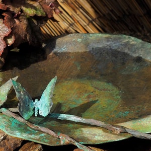 May include: A rustic, green metal bird bath with a hammered finish. Three metal butterflies are attached to the rim of the bath.
