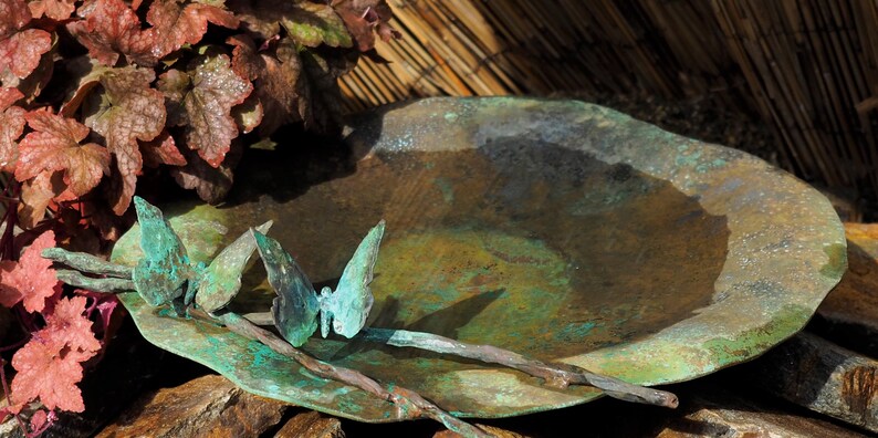 May include: A rustic, green metal bird bath with a hammered finish. Three metal butterflies are attached to the rim of the bath.