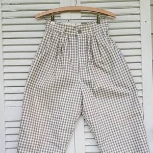 May include: A pair of beige and brown checkered pants with pleats hanging on a wooden hanger.