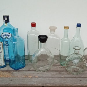 May include: A collection of nine glass bottles, some with blue liquid, some clear, and some with blue, gold, or red caps. The bottles are arranged on a wooden surface.