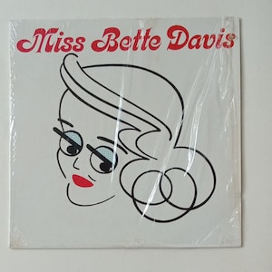 May include: A white background with black line art of a woman's face with red lips and the text "Miss Bette Davis" in red cursive.