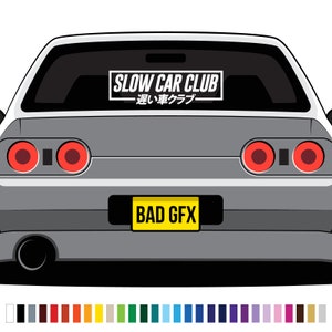May include: A grey car with a black and white sticker that says "SLOW CAR CLUB - 遅い車クラブ" on the rear window. The car has a yellow number plate that says "BAD GFX".