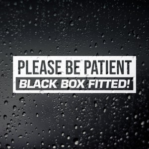 May include: A white rectangular sticker with the words "PLEASE BE PATIENT" and "BLACK BOX FITTED!" in a bold, sans-serif font. The background is a dark, wet surface with water droplets.