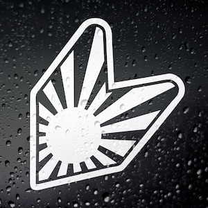 以下が含まれることがあります： 車のリアウィンドウスポイラーの形をした昇る太陽のデザインの白いビニールステッカー