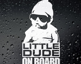 May include: White vinyl sticker featuring a cartoon baby wearing sunglasses and a beanie. The text "LITTLE DUDE ON BOARD" is below the baby.