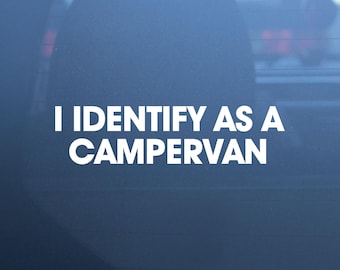 May include: A white vinyl decal applied to a dark blue glass surface, featuring the bold, sans-serif text "I IDENTIFY AS A CAMPERVAN" arranged in two lines. The lettering is clean, opaque, and clearly legible against the dark background.